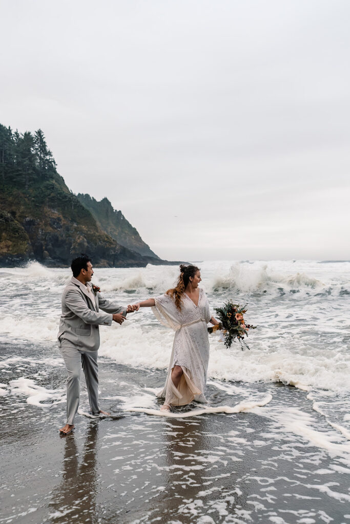 a bride and groom rush out of the waves following their elopement ceremony. 