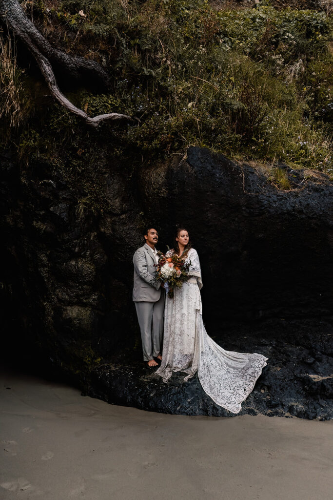 after their elopement ceremony, a bride and groom embrace while standing on a large basalt rock. moss lines the space above them 