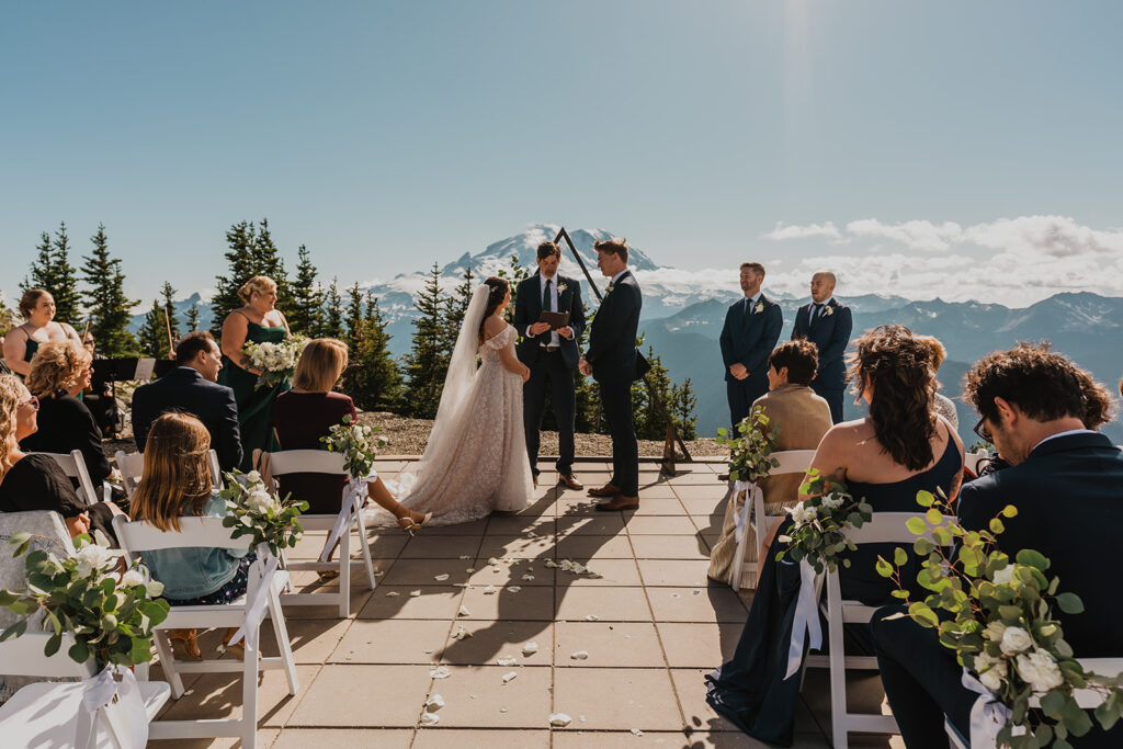 an officiant speaks during a mountain elopement ceremony. Mount Rainier is clearly seen in the background. their guests frame the foreground 