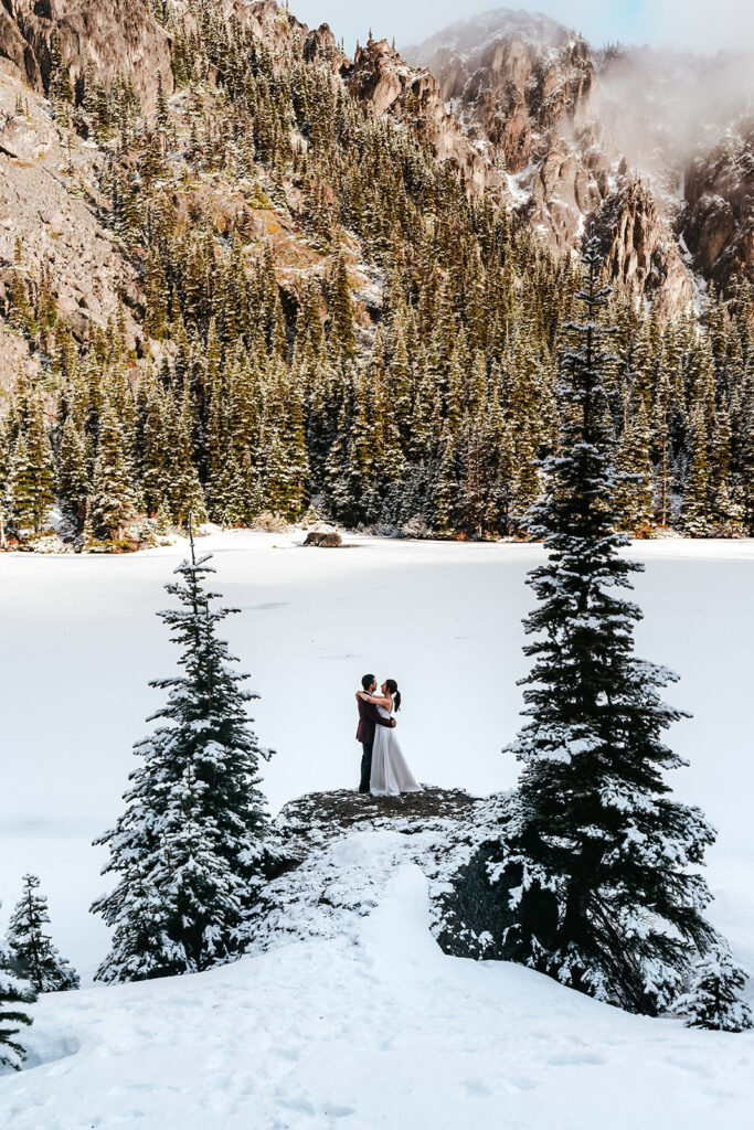 a bride and groom embrace during their elopement ceremony in a snowy landscape. they are perfectly framed between two pine tress. 