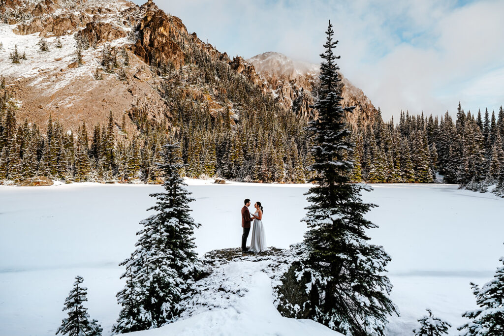 during their elopement ceremony, a bride and groom exchange vows in a snowy landscape. they are perfectly framed between two pine trees