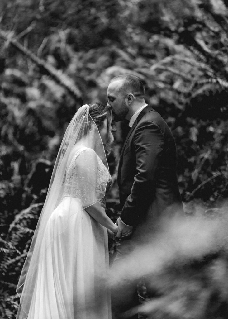 a groom kisses the top of his brides head as they embrace during their forest elopement ceremony