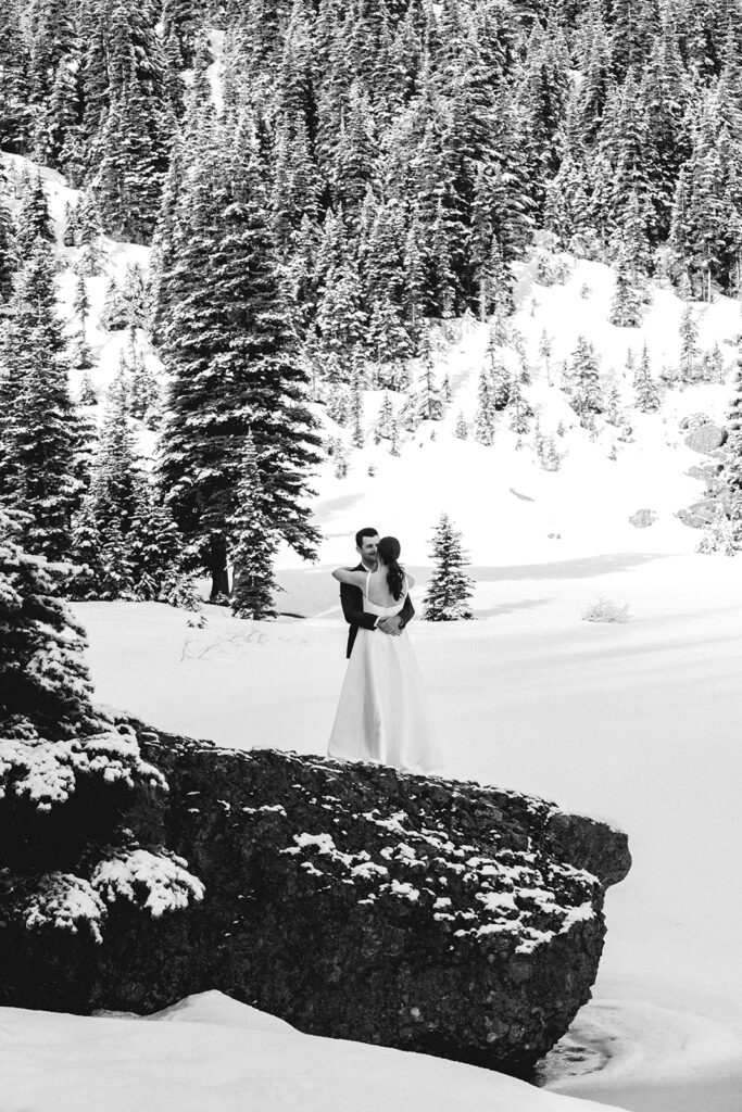 a black and white photo of a bride and groom embracing in a snowy landscape during their elopement ceremony 