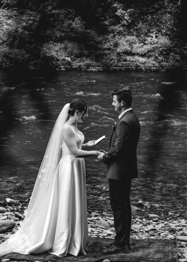 a bride reads her vows to her groom during their elopement ceremony by a flowing river 