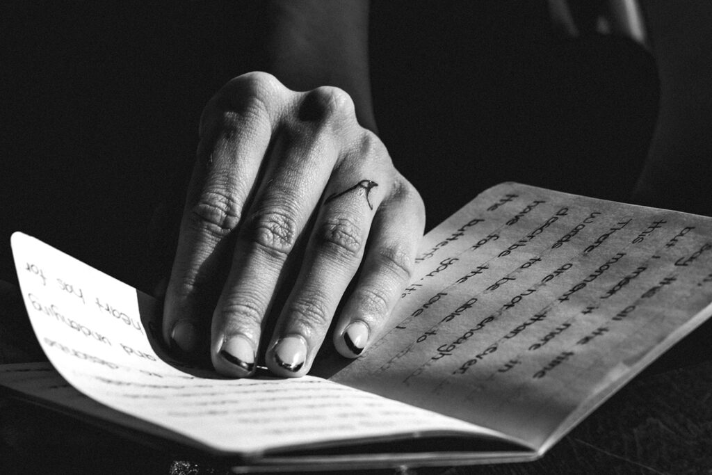 a black and white photo of a brides hand flipping through her vow book as she prepares for her elopement ceremony