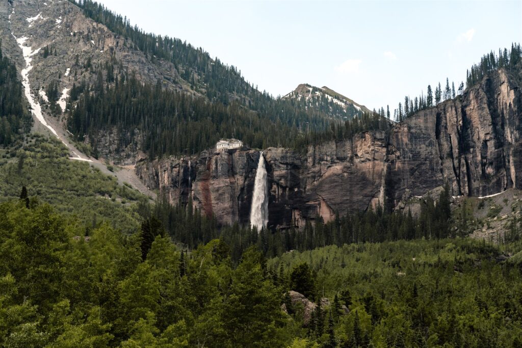 A landscape shot of the waterfall of their sunrise elopement location, a gushing waterfall surrounded by green trees and red canyon rocks.