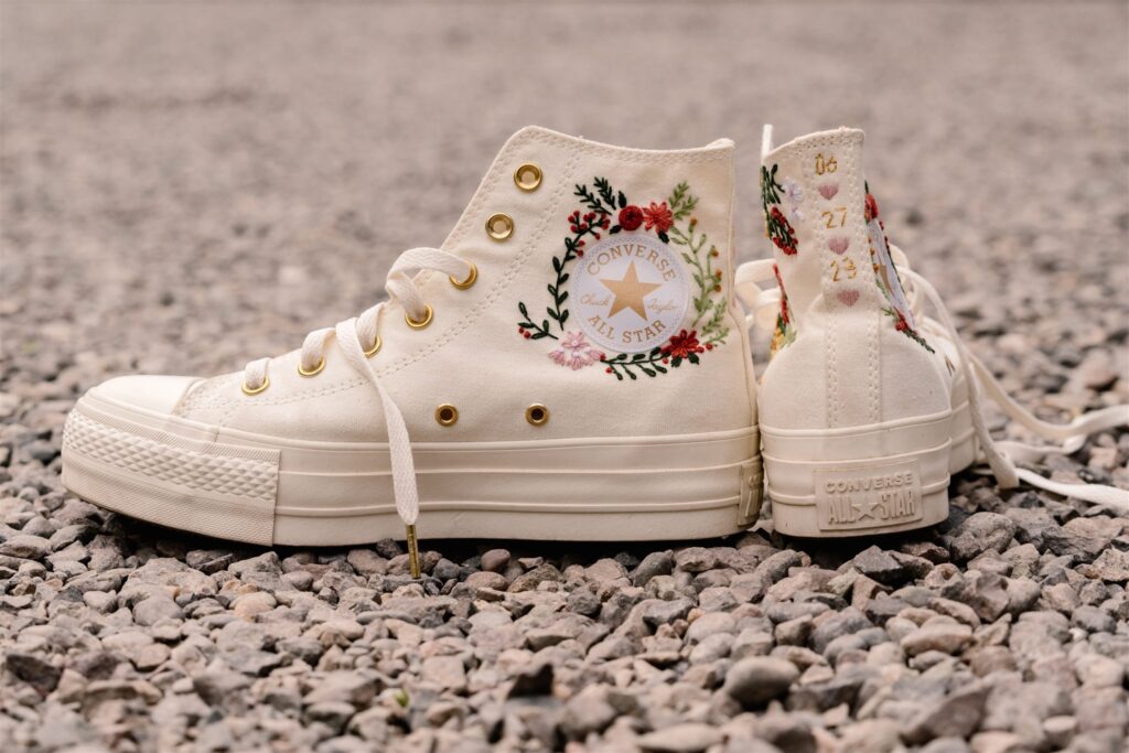 detail shot of our brides white converse wedding shoes. Complete with custom embroidery detailing their date, initials, and wildflowers that match her veil.