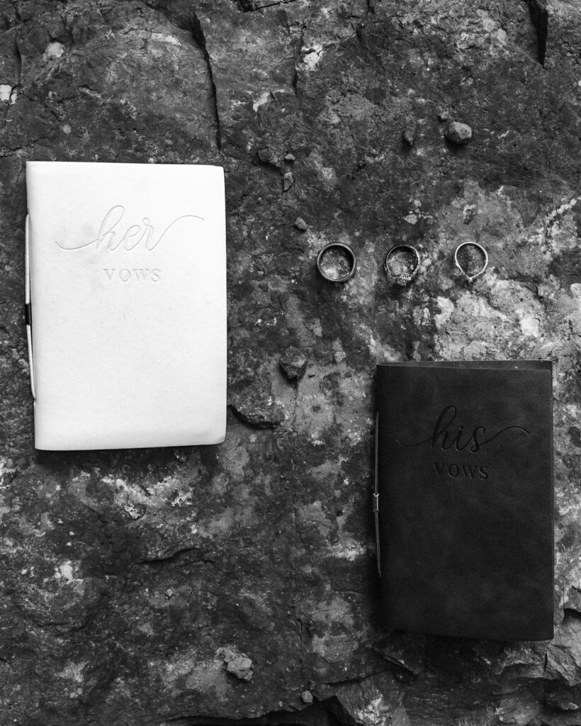 Black and white shot of vow books and wedding rings rest on a rock