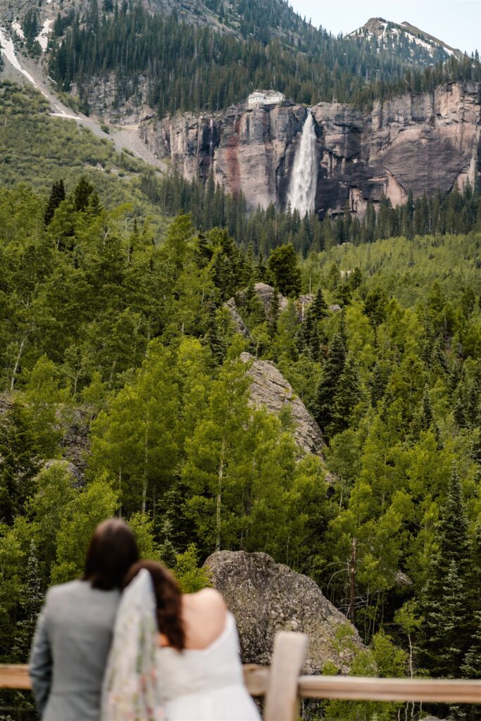 Couple in wedding attire gazes at the the waterfall they will soon journey to for their sunrise elopement