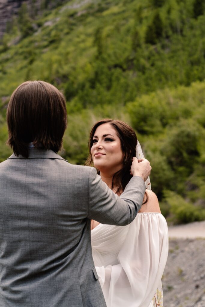 A couple in wedding attire stand gazing at each other. The groom brushes the brides hair back during their sunrise elopement.