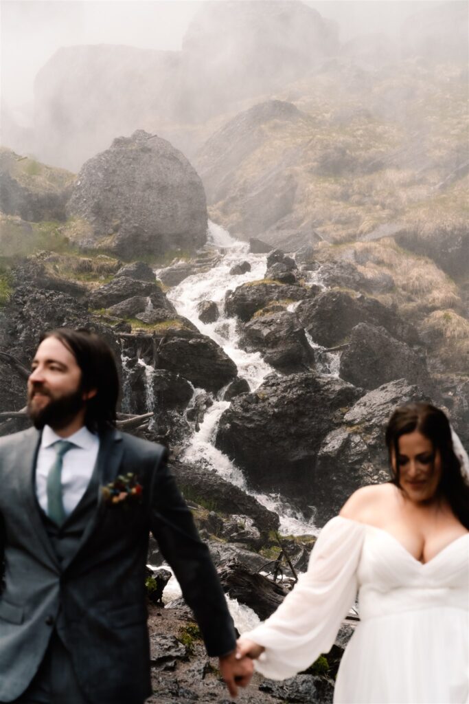 A bride and groom in wedding attire, frame a zig-zagging waterfall during their sunrise elopement