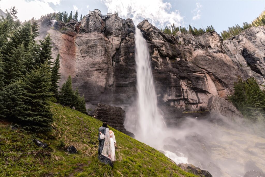 A wide landscape shot of a bride and groom gaze at the powerful falls they exchanged vows under during their sunrise elopement.