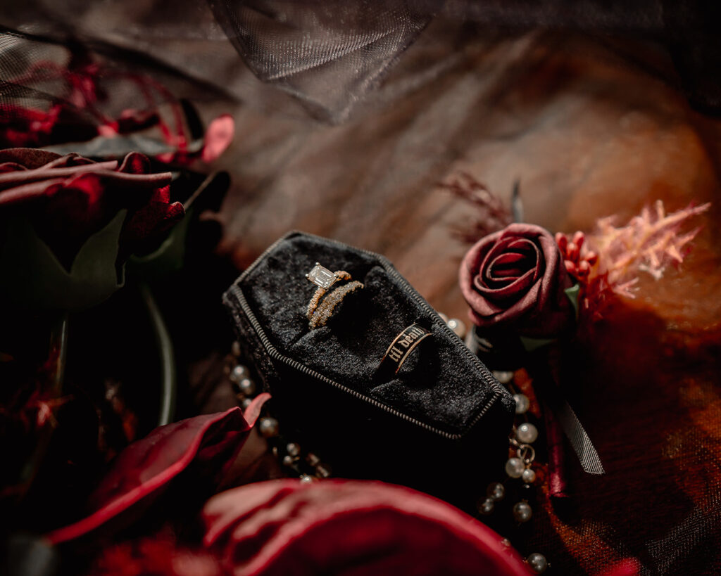 a detail image of this moody pacific northwest elopement wedding details including wedding rings resting in a velvet coffin ring box, a red and black boutonnière.