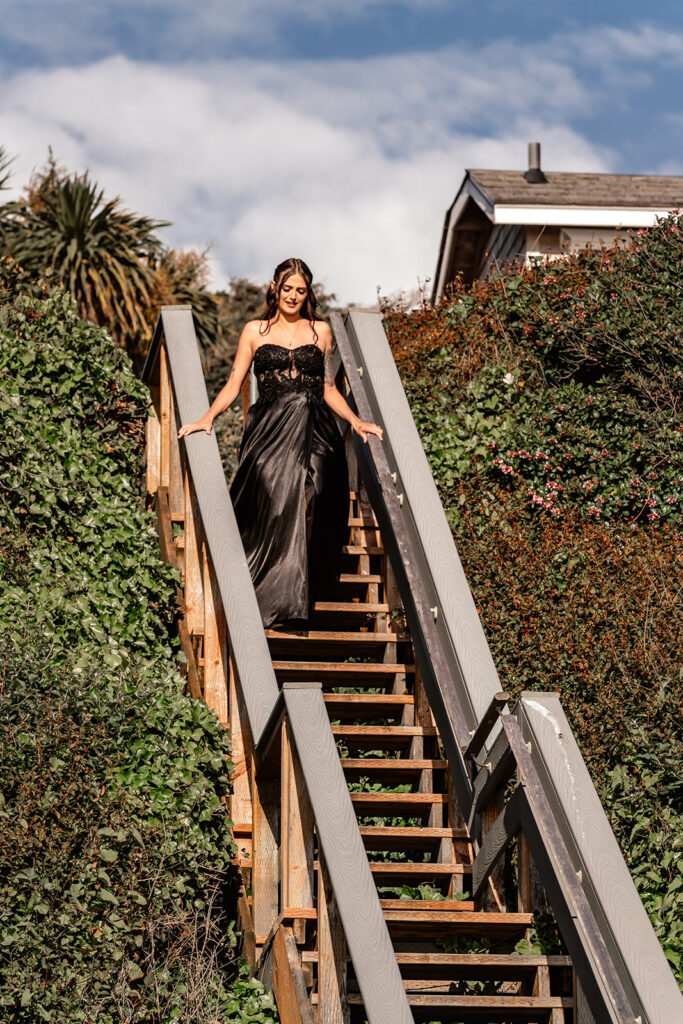 a bride in an all black wedding dress walks down wooden steps to meet her groom for their pacific northwest elopement