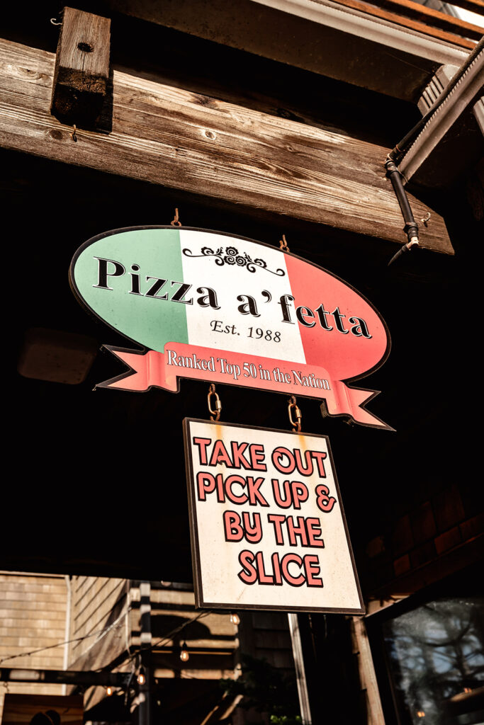 a green, white, and red sign for a pizza parlor reading "pizza a'fetta"