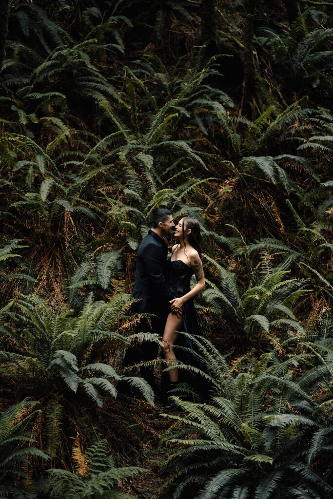 A couple in all black wedding attire embrace in a moody rainforest during their pacific northwest elopement