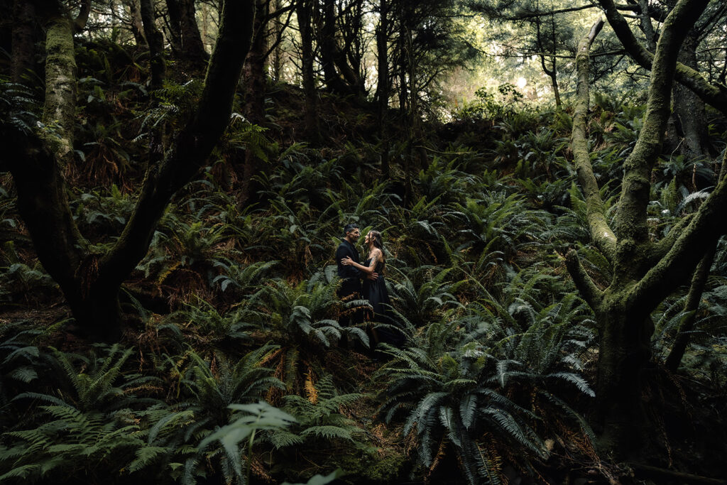 A couple in all black wedding attire embrace in a moody rainforest during their pacific northwest elopement