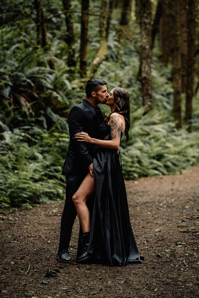 A couple in all black wedding attire embrace in a moody rainforest during their pacific northwest elopement