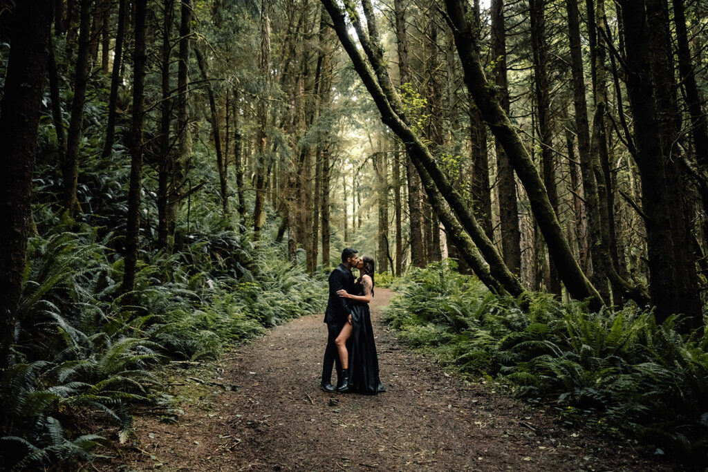 A couple in all black wedding attire kiss in a moody rainforest during their pacific northwest elopement