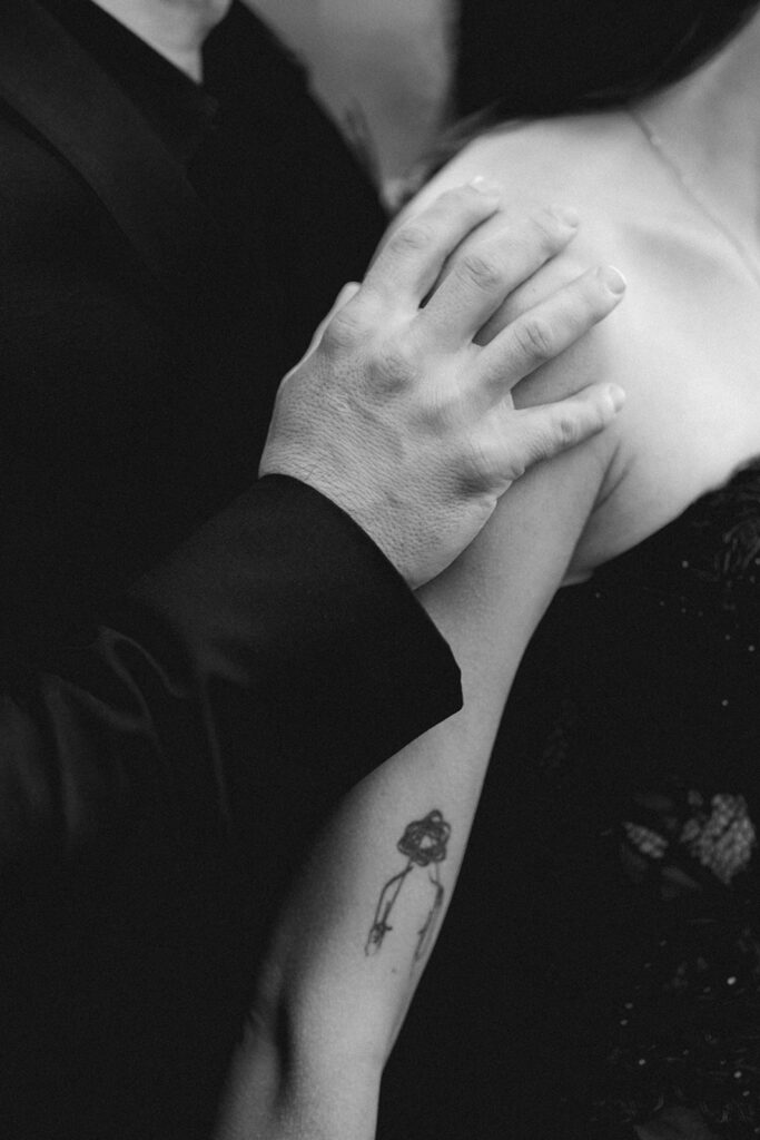 a black and white detail shot of a grooms hand on his brides arm c 