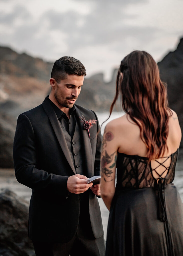 a groom reads his vows to his bride on a moody beach during their pacific northwest elopement