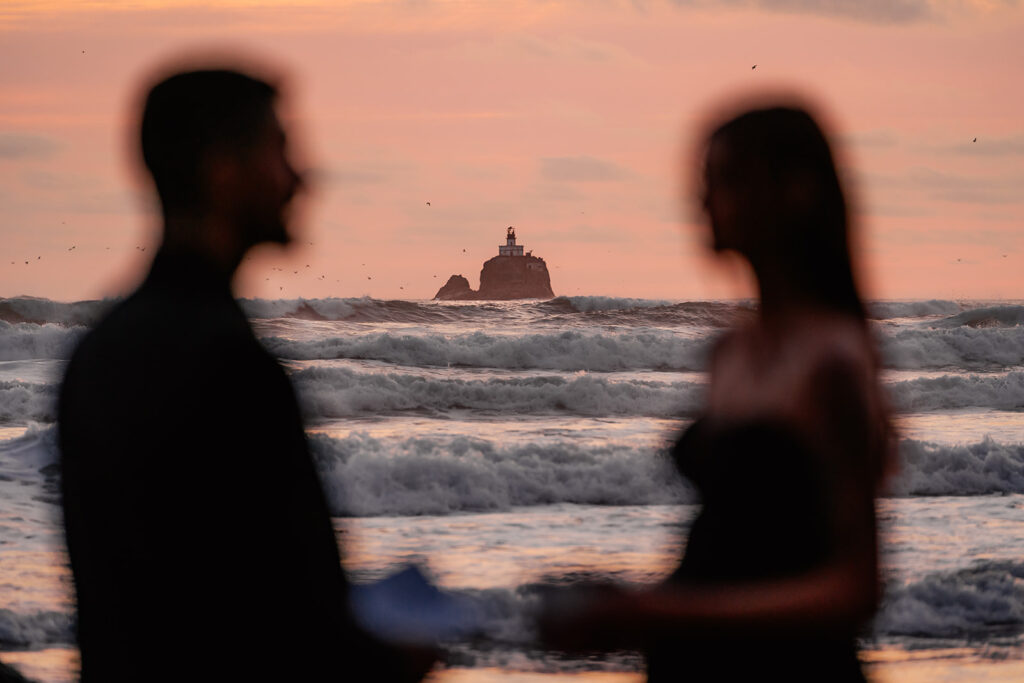 a shot of a faraway lighthouse in a pink sunset framed by the blurred silhouette of a couple