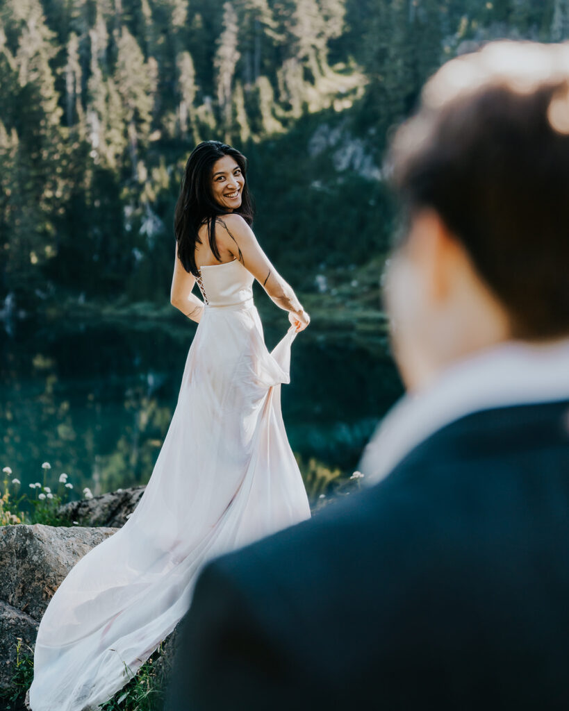 an over the shoulder shot of a bride in her wedding dress. She smiles widely at her groom during their hiking elopement