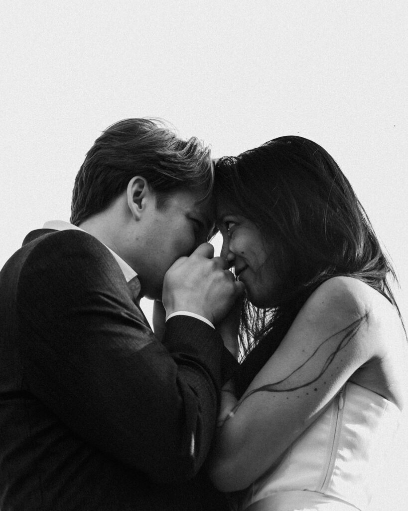 a black and white photo of a couple in their wedding attire. it is a close up shot, shooting upwards and playing with the cloudless sky