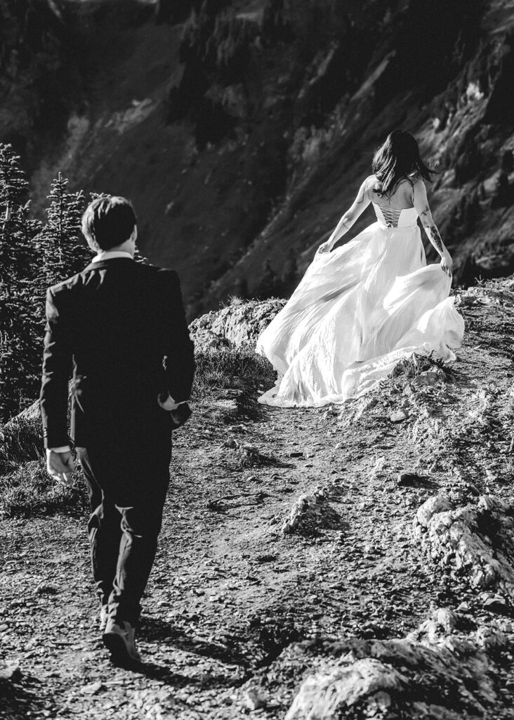 a black and white image of a bride and groom exploring the mountains in their wedding attire during their hiking elopement