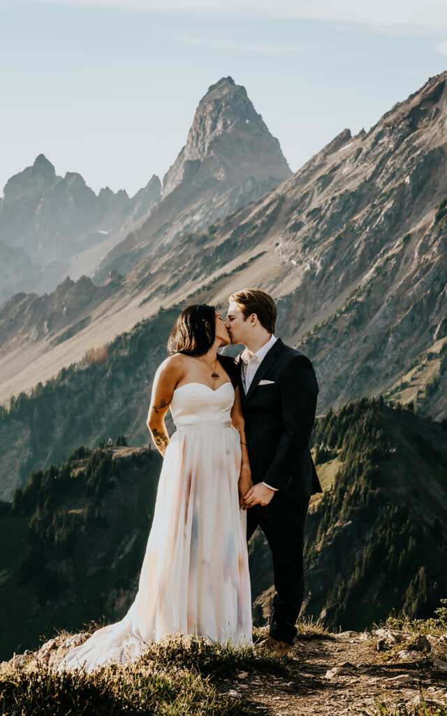 a bride and groom embrace in their wedding attire. A sweeping mountain range serves as their backdrop for this hiking elopement