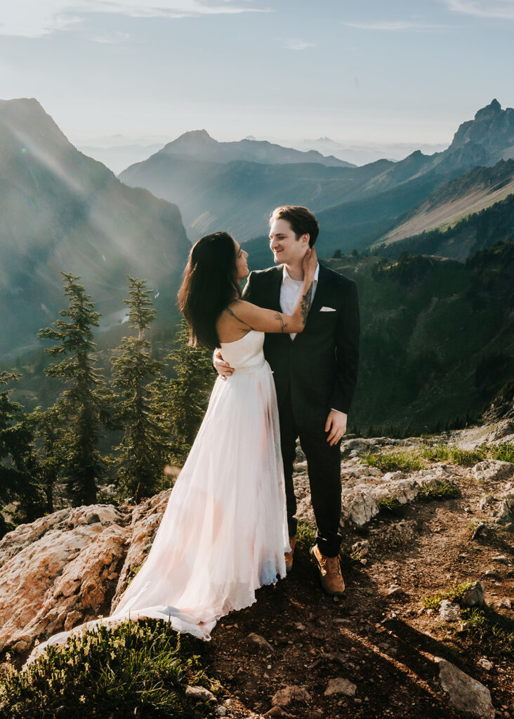 a bride and groom embrace in their wedding attire. A sweeping mountain range serves as their backdrop for this hiking elopement