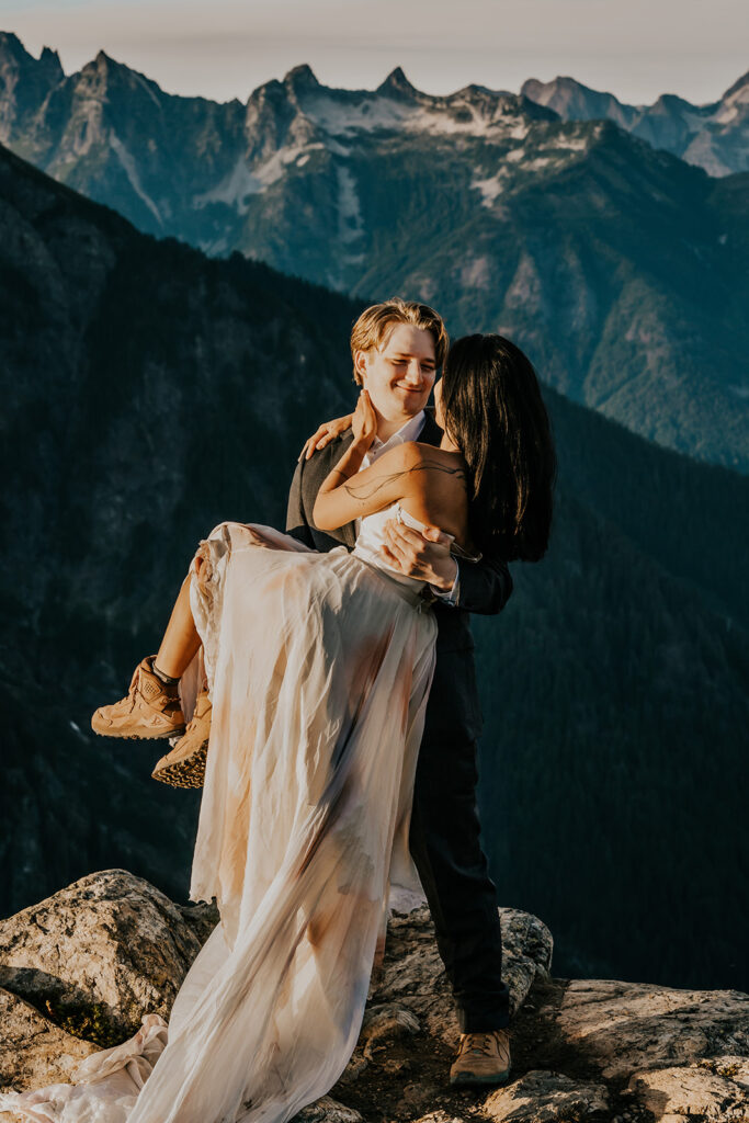 a groom scoops up his bride and smiles widely at her. Her dress billows beneath her