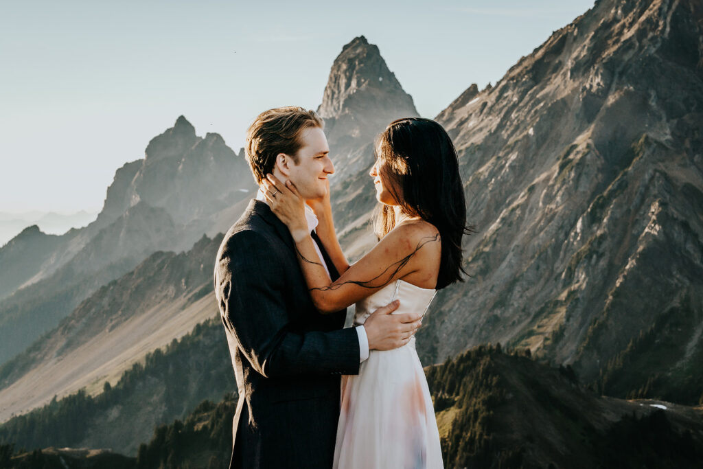 a bride and groom embrace in their wedding attire. There are beautiful mountains i the backdrop during their hiking elopement