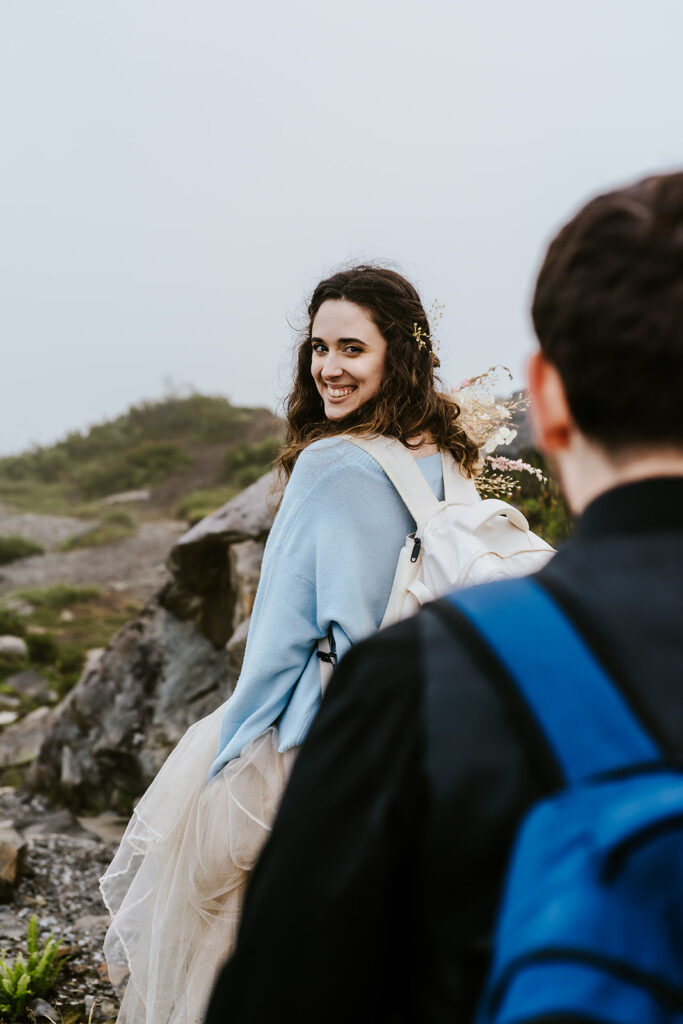 shot over the shoulder of her groom, we see his perspective as his bride turns and smiles widely at her groom as they hike during their North Cascades elopement