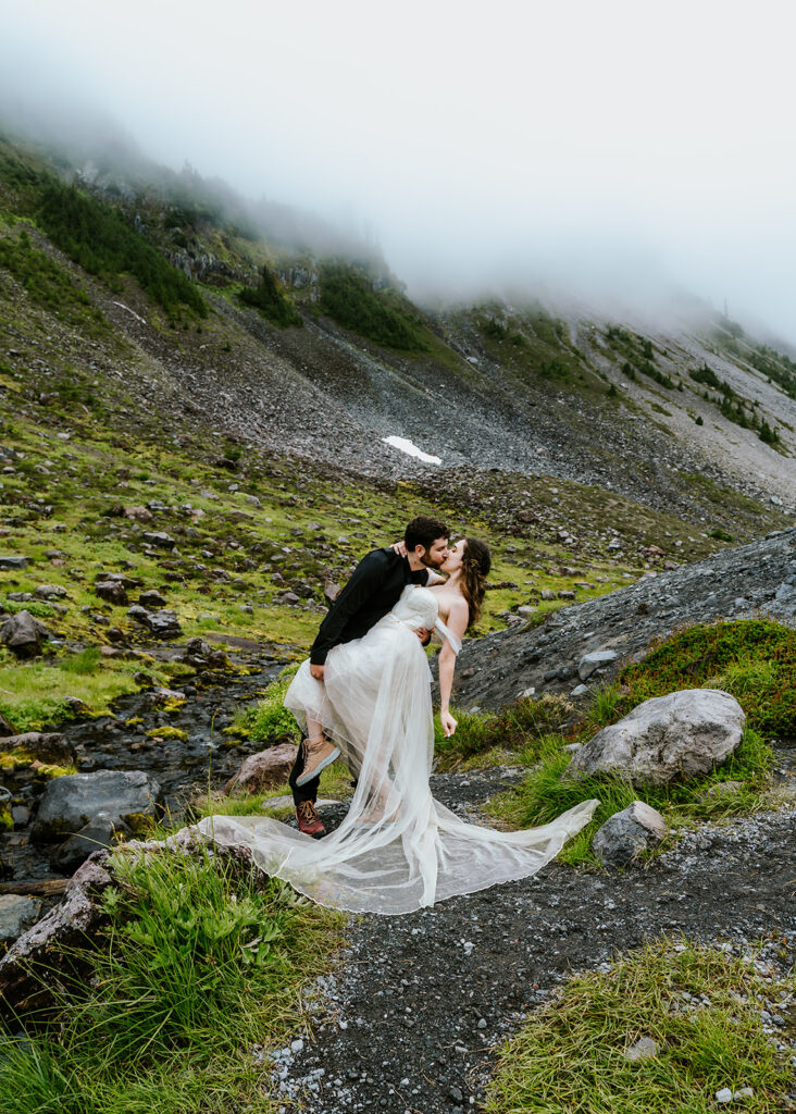 a bride and groom do a dip kiss in front of a beautiful green landscape during their north cascades elopement