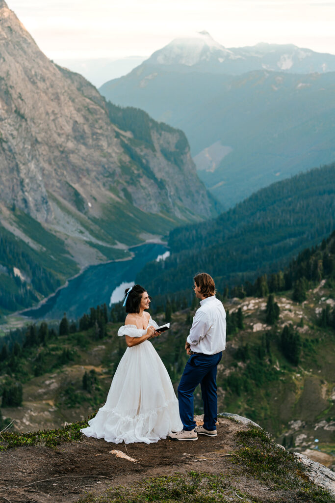 for their north cascades elopement, a bride and groom exchange vows at an overlook. from their ceremony location, we see the valley below them, and the towering mountains behind them. 