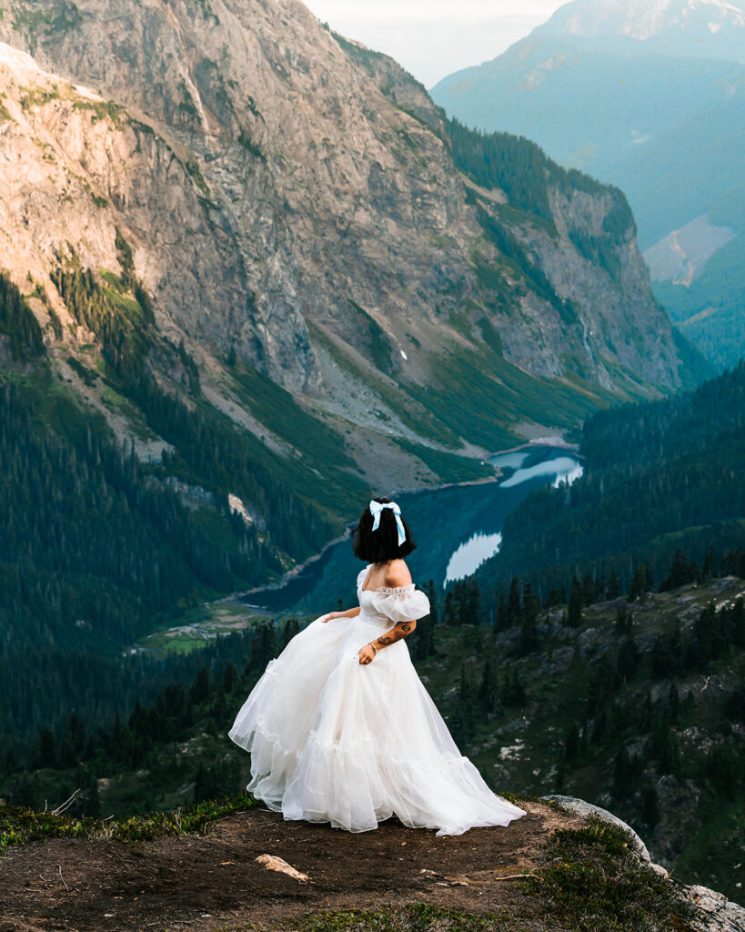 a bride twirls her dress and gazes out at the valley below her and the mountains above her during her north cascades elopement