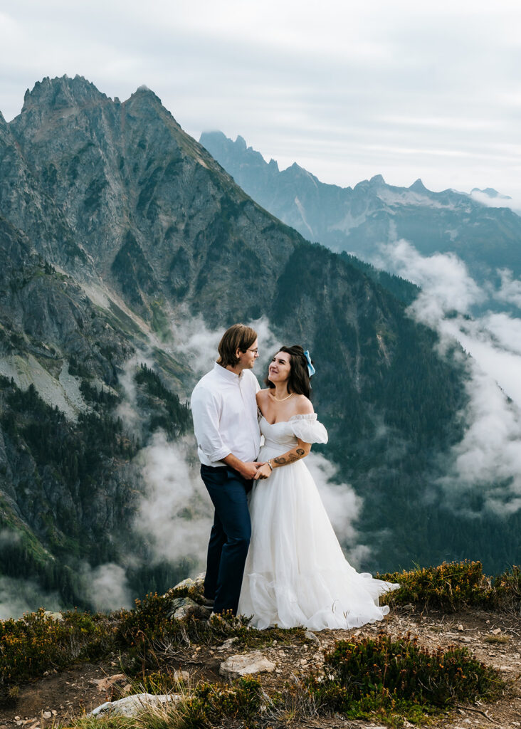 a bide and groom in wedding attire gaze lovingly at each other as the mountains rise behind them during their north cascades elopement