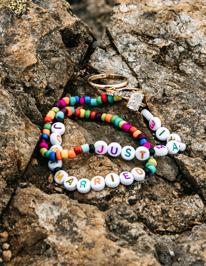 a detail shot of handmade friendship style bracelets that read "just married" and wedding bands, scattered on a rock from this north cascades elopement