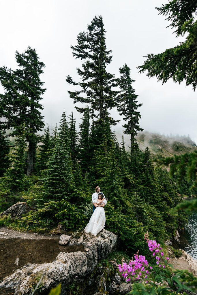 a bride and groom embrace in front of tall, green trees during their north cascades elopement