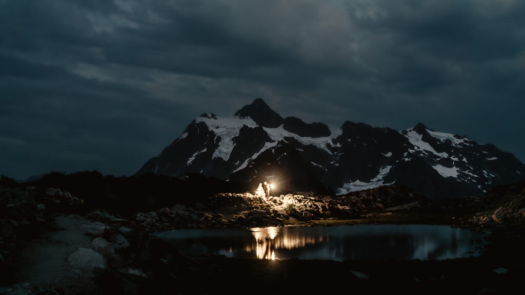 a landscape shot of a bride and groom exploring a mountain and tarn with lanterns during dusk during their north cascades elopement