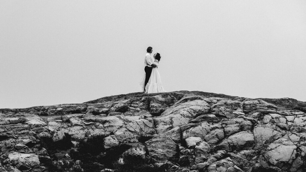 a black and white photo of a couple embracing on a large rock formation surrounded by fog during the north cascades elopement