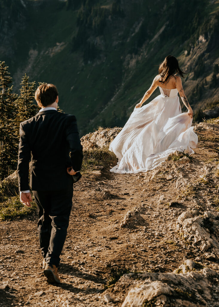 a bride leading her groom to a rocky outcropping. her dress billows behind her during their north cascades elopement