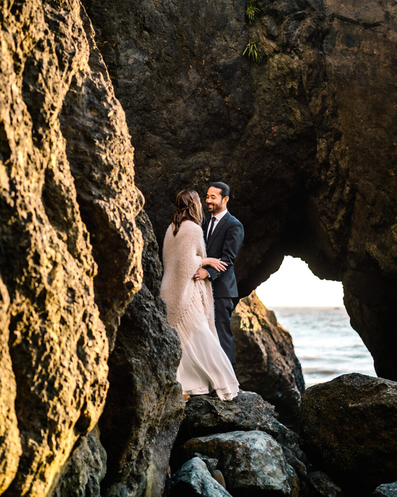 a groom smiles at his bride as they embrace on a sea stack during their ruby beach elopement 