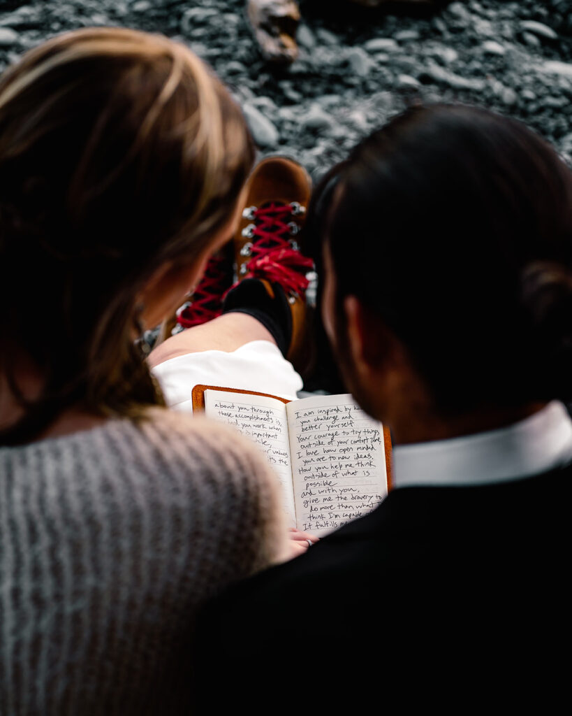 an over the should shot of their vows as they read them together during their ruby beach elopement. the pages of the vows are framed by their faces