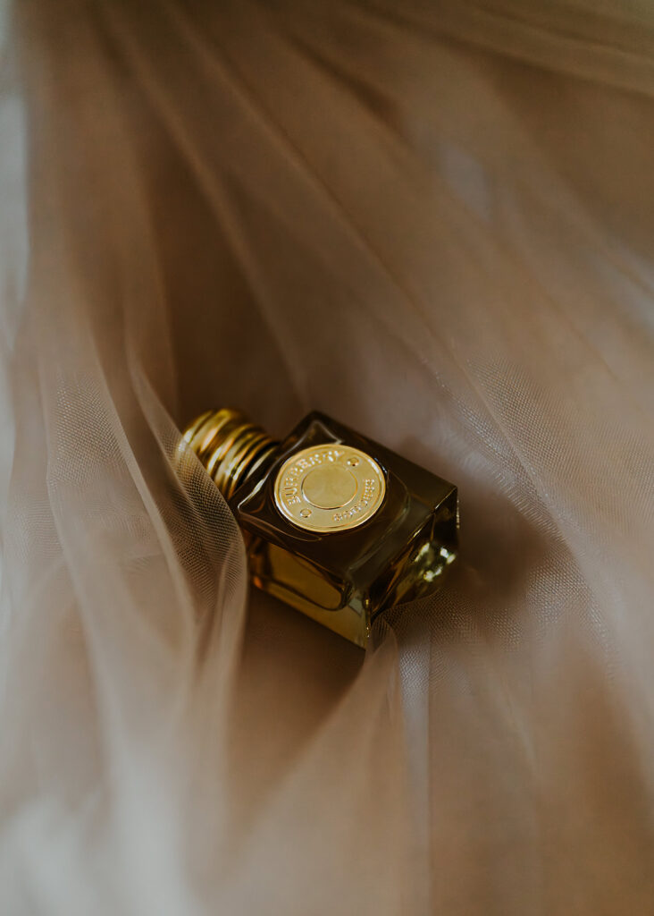 a detail shot of the perfume used by our bride. it lays casually on top of the gauzy fabric of her wedding cape.