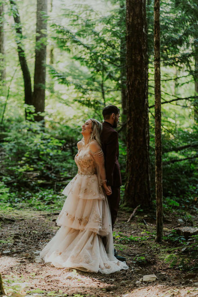 a bride and groom stand back to back smiling with anticipation as they prepare for their first look