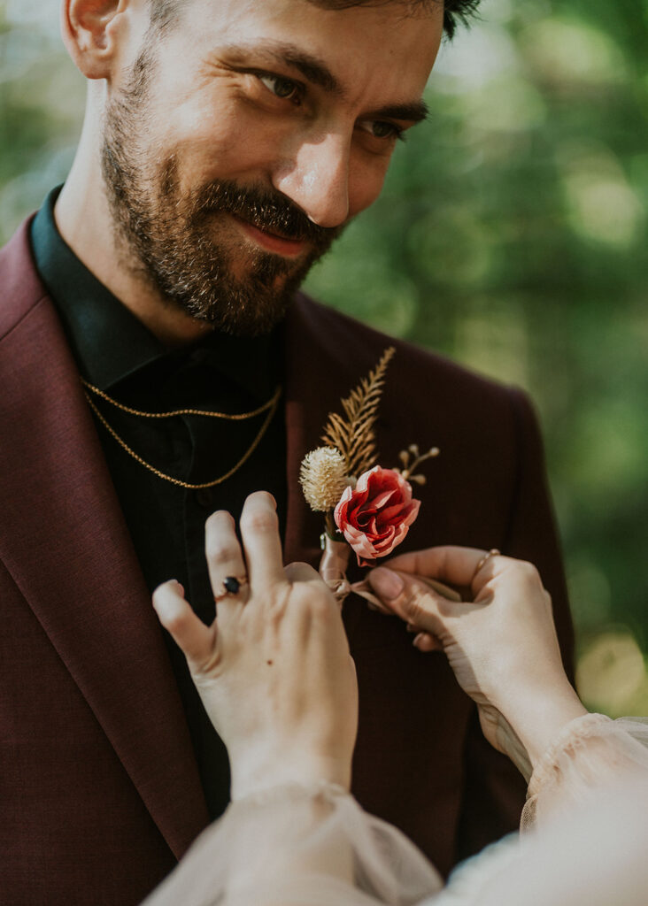 a groom gazes sweetly at his bride as she pins his boutonniere onto his lapel