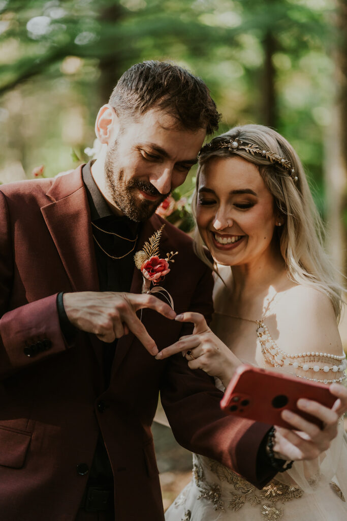 after their first look, a bride and groom take a selfie while making a heart with their hands