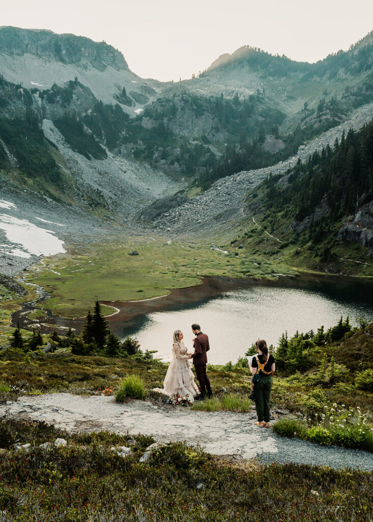 a bride and groom exchange vows on a beautiful trail with a shimmering lake below them during their mount baker elopement